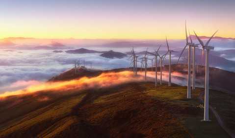 Wind turbines on top of a mountain with fog below.
