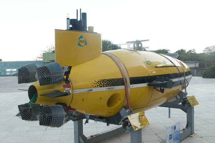 A yellow underwater vehicle is mounted on a stand ashore